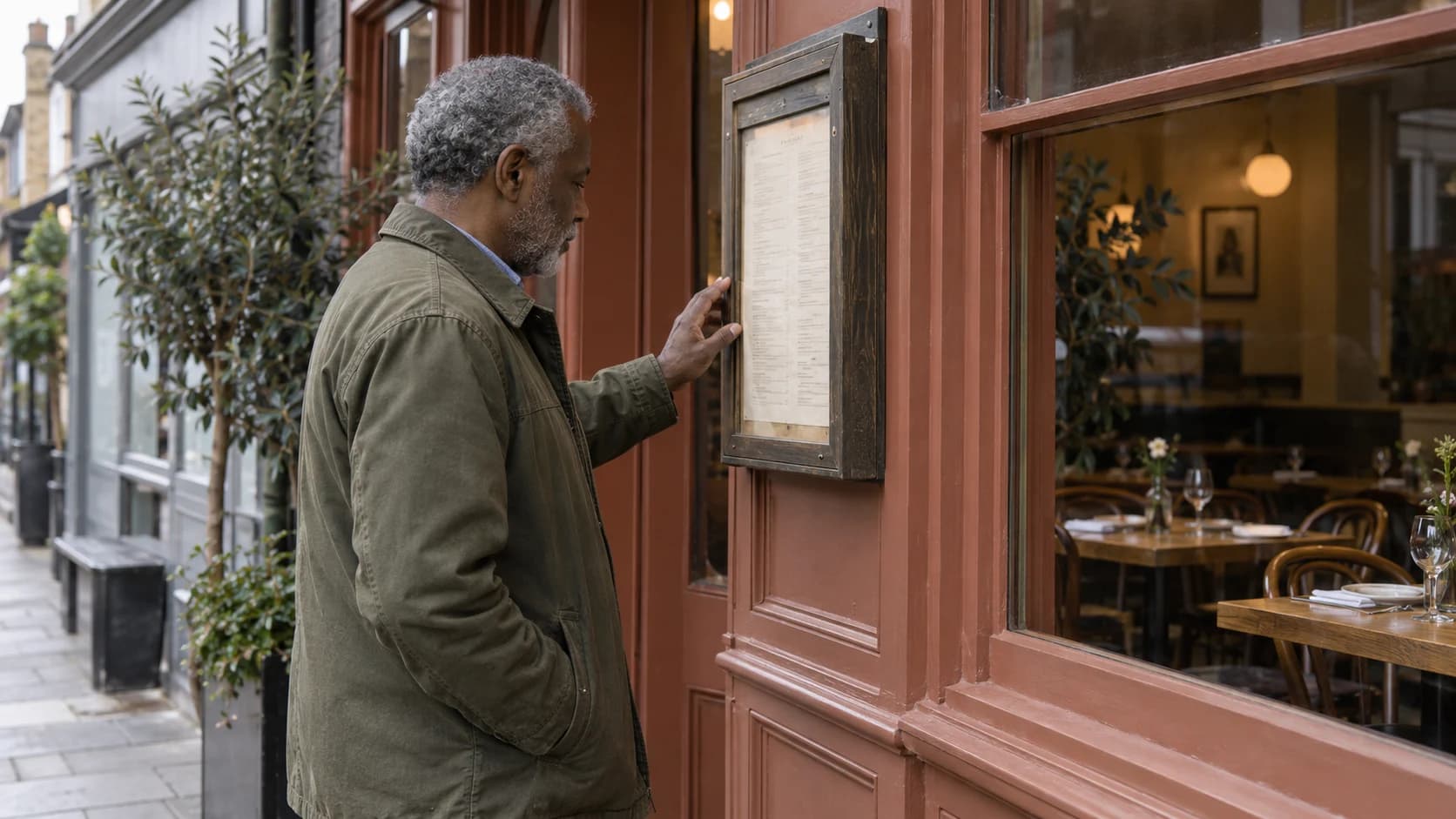 A customer consulting an unreadable menu beside a terracotta-painted restaurant entrance.