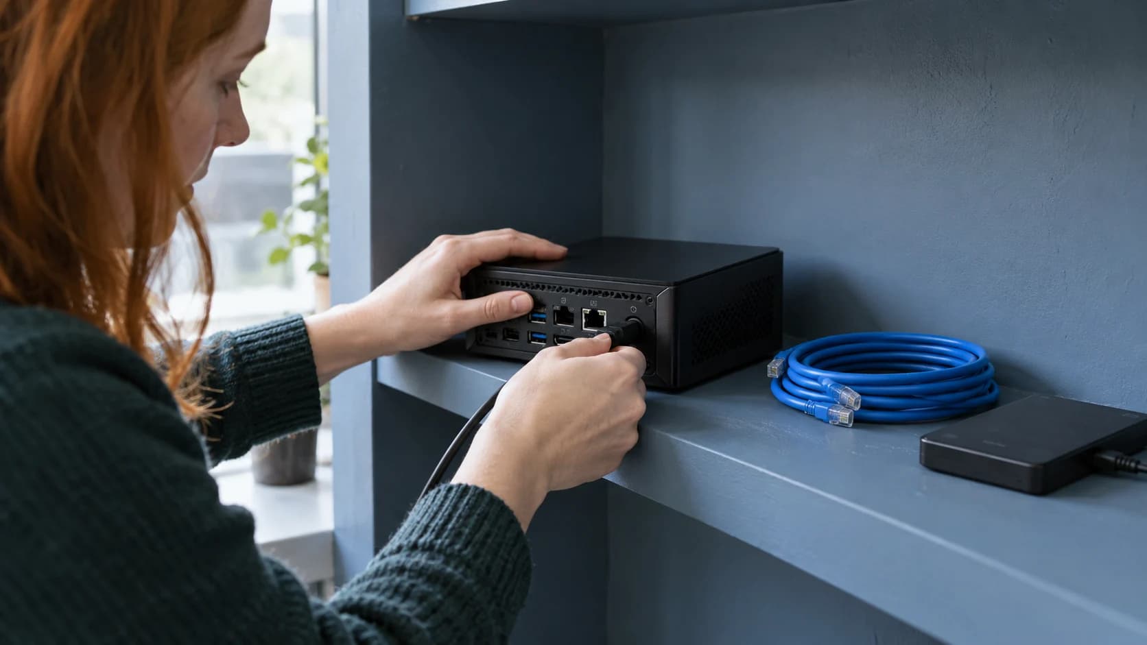 A compact computer and network cable being prepared on a painted shelf.